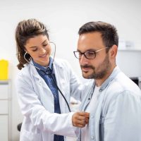 Young doctor is using a stethoscope listen to the heartbeat of the patient. Shot of a female doctor giving a male patient a check up
